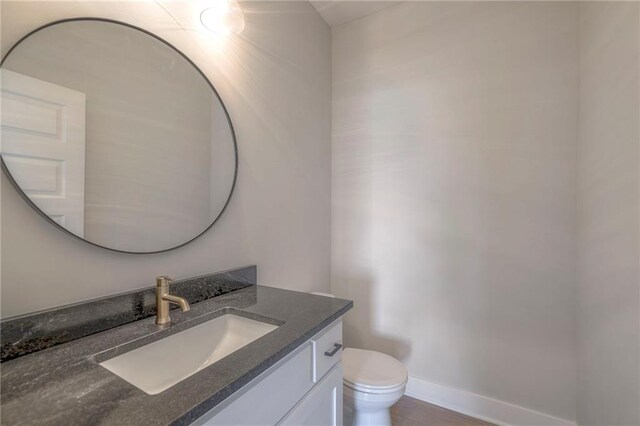 half bath with toilet, vanity, baseboards, and wood finished floors