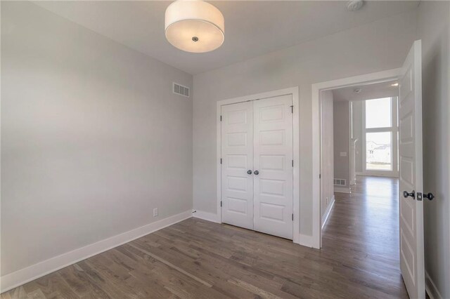 unfurnished bedroom with dark wood-type flooring, a closet, visible vents, and baseboards