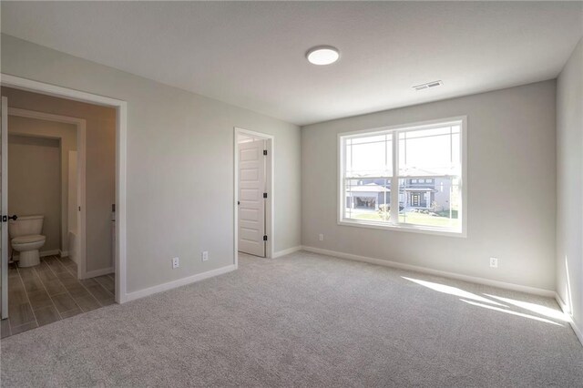 unfurnished bedroom featuring baseboards, visible vents, carpet flooring, and ensuite bathroom