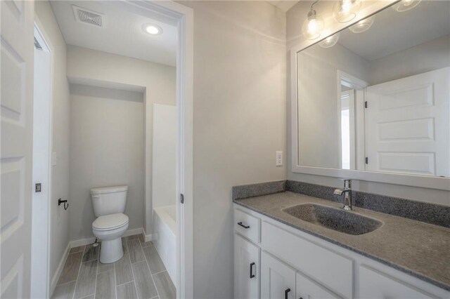 bathroom featuring baseboards, visible vents, toilet, a tub, and vanity