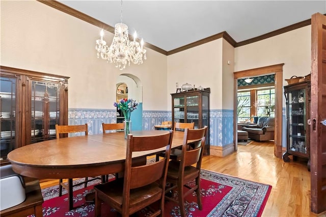 dining space featuring crown molding, light wood-type flooring, a notable chandelier, and a towering ceiling