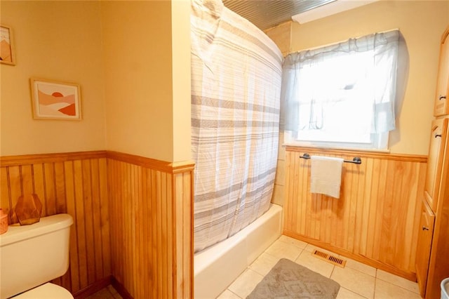 bathroom featuring tile patterned flooring, shower / bath combination with curtain, toilet, and wood walls