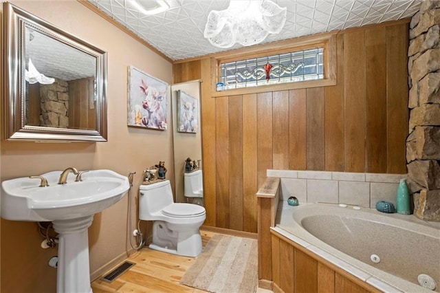 bathroom featuring a chandelier, toilet, a bathing tub, wood walls, and wood-type flooring