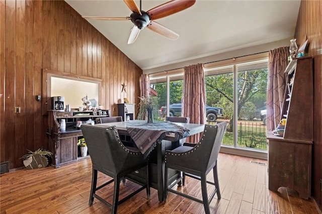 dining area with high vaulted ceiling, hardwood / wood-style flooring, wooden walls, and ceiling fan