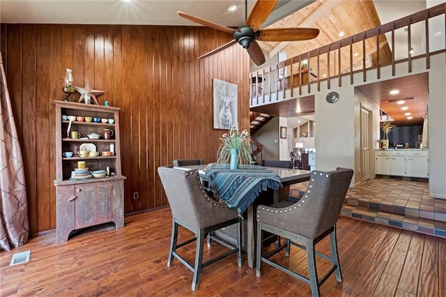 dining area with wooden walls, ceiling fan, wood-type flooring, and high vaulted ceiling