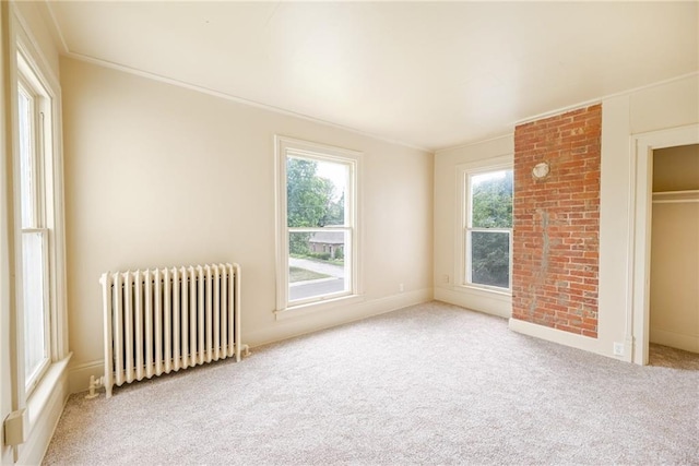 unfurnished bedroom with radiator heating unit, multiple windows, light carpet, and ornamental molding