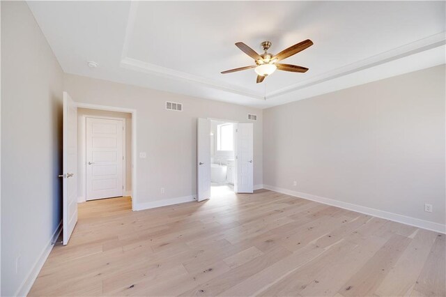 7004 NE 102nd Ct, Kansas City, MO 64156 - unfurnished bedroom featuring a tray ceiling, light wood-style floors, connected bathroom, and a ceiling fan
