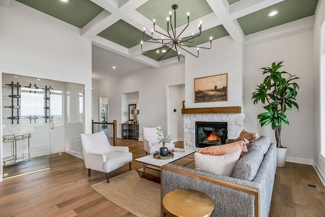 living room featuring beam ceiling, a chandelier, a fireplace, coffered ceiling, and hardwood / wood-style flooring