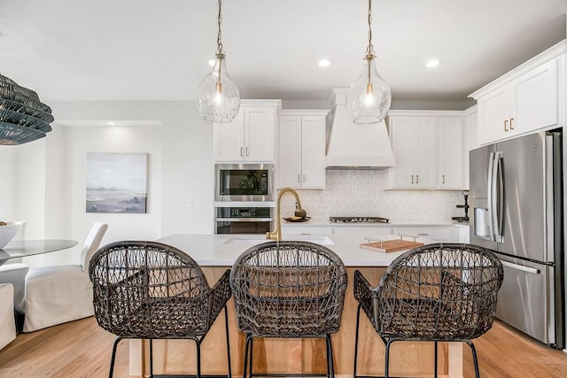 kitchen with appliances with stainless steel finishes, light hardwood / wood-style flooring, premium range hood, decorative backsplash, and a kitchen breakfast bar