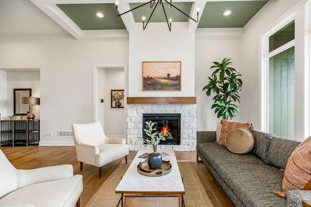 living room featuring beamed ceiling, a fireplace, a chandelier, and hardwood / wood-style floors