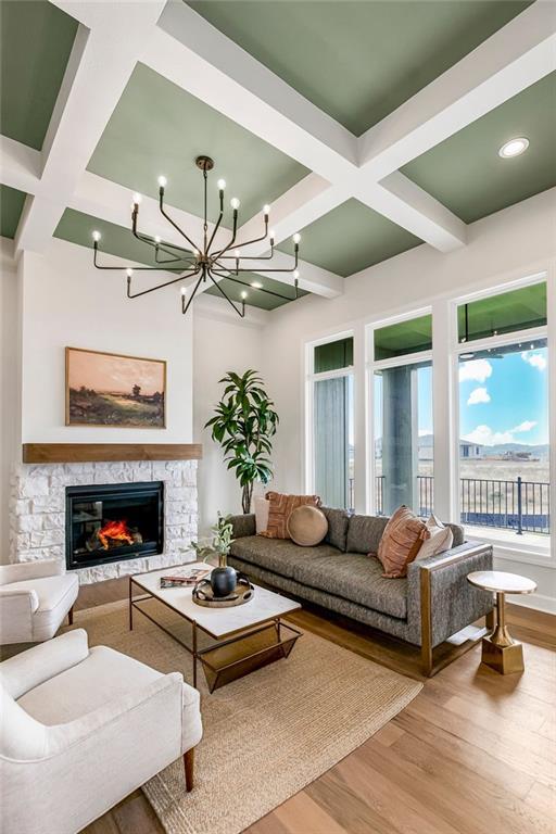 living room with beamed ceiling, wood-type flooring, a stone fireplace, and coffered ceiling