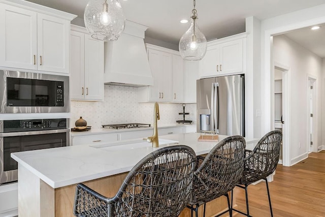 kitchen with white cabinetry, stainless steel appliances, an island with sink, and premium range hood