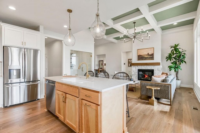 kitchen with a stone fireplace, sink, light wood-type flooring, appliances with stainless steel finishes, and an island with sink