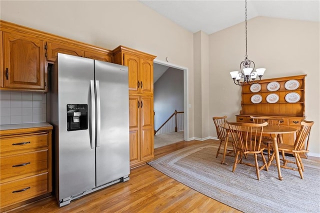 kitchen featuring pendant lighting, stainless steel refrigerator with ice dispenser, vaulted ceiling, decorative backsplash, and light hardwood / wood-style floors