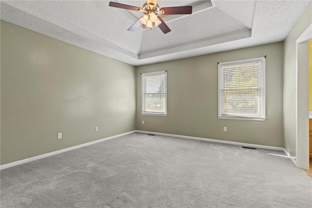 unfurnished room with ceiling fan, light colored carpet, and a tray ceiling