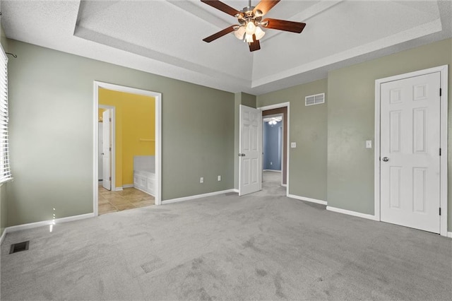 unfurnished bedroom with a tray ceiling, ensuite bath, ceiling fan, and light colored carpet