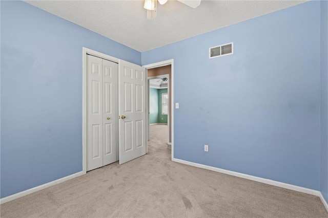 unfurnished bedroom with ceiling fan, a closet, light colored carpet, and a textured ceiling