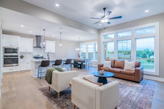 living room featuring ceiling fan with notable chandelier, plenty of natural light, and light hardwood / wood-style floors