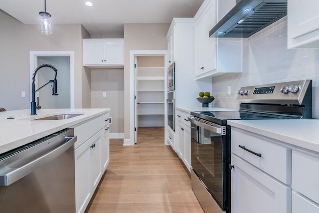 kitchen with hanging light fixtures, wall chimney exhaust hood, white cabinetry, appliances with stainless steel finishes, and light hardwood / wood-style floors