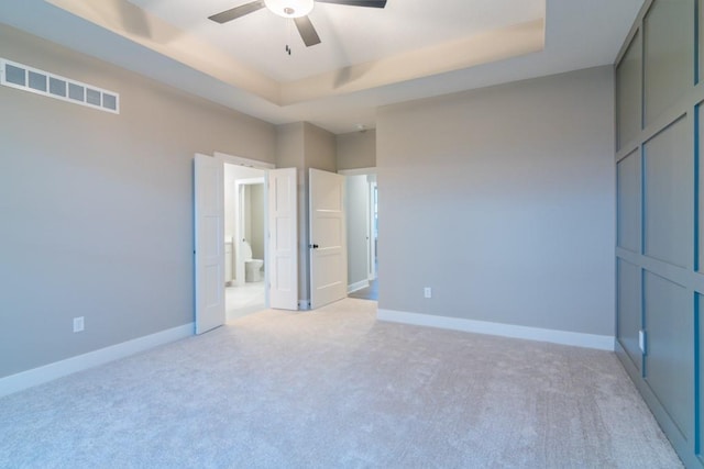 unfurnished bedroom featuring ceiling fan, a raised ceiling, and light carpet