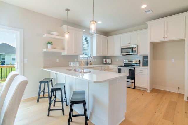 kitchen with decorative backsplash, light wood-type flooring, stainless steel appliances, pendant lighting, and white cabinetry