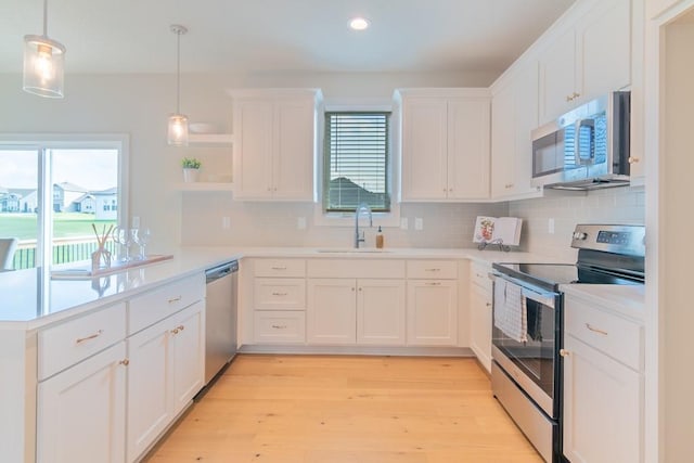 kitchen with pendant lighting, white cabinets, sink, appliances with stainless steel finishes, and light hardwood / wood-style floors