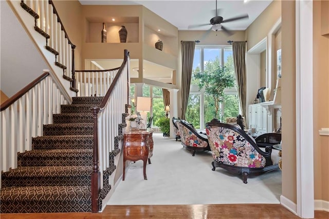 stairway featuring a towering ceiling, baseboards, a ceiling fan, and wood finished floors