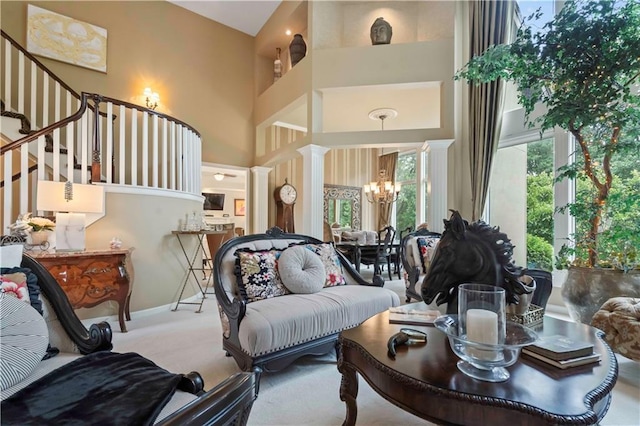 carpeted living room with a notable chandelier, a towering ceiling, ornate columns, and stairs