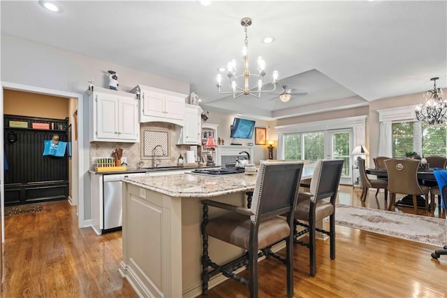 kitchen with decorative backsplash, an inviting chandelier, appliances with stainless steel finishes, wood finished floors, and a kitchen bar