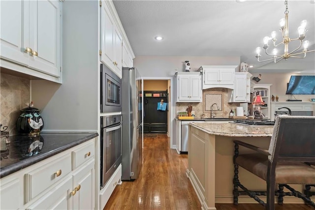 kitchen featuring light stone counters, decorative backsplash, appliances with stainless steel finishes, white cabinetry, and wood finished floors