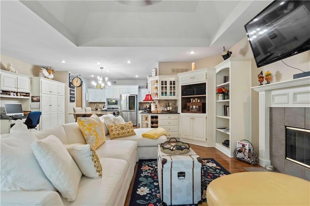 living area with dark wood-style floors, a notable chandelier, recessed lighting, a raised ceiling, and a tiled fireplace