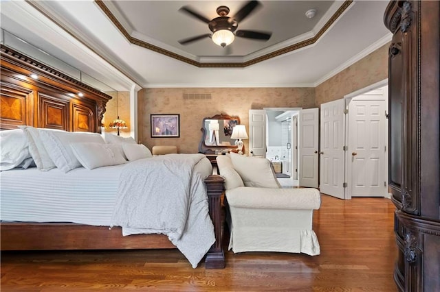 bedroom with crown molding, a raised ceiling, visible vents, a ceiling fan, and wood finished floors