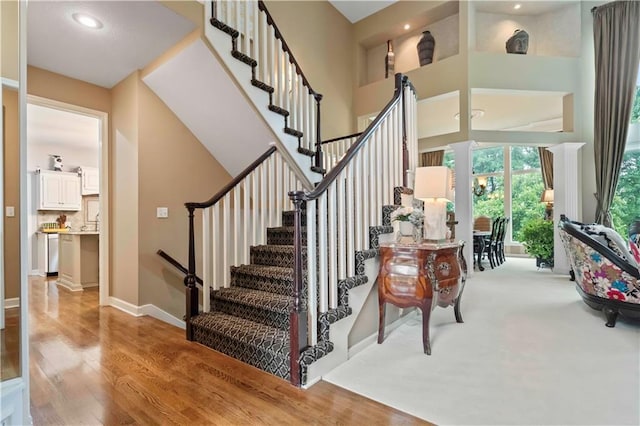 stairway featuring a high ceiling, recessed lighting, wood finished floors, and baseboards