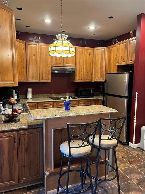 kitchen featuring cooktop, ventilation hood, light stone counters, stainless steel fridge, and dark tile patterned flooring