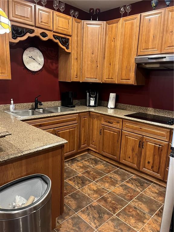 kitchen featuring black electric cooktop, extractor fan, sink, light stone counters, and dark tile patterned flooring