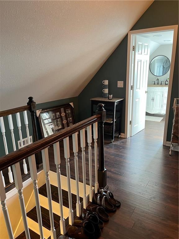 staircase with a textured ceiling, hardwood / wood-style flooring, and lofted ceiling