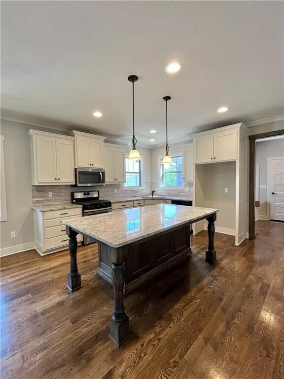 kitchen with appliances with stainless steel finishes, white cabinets, dark hardwood / wood-style floors, and a kitchen island