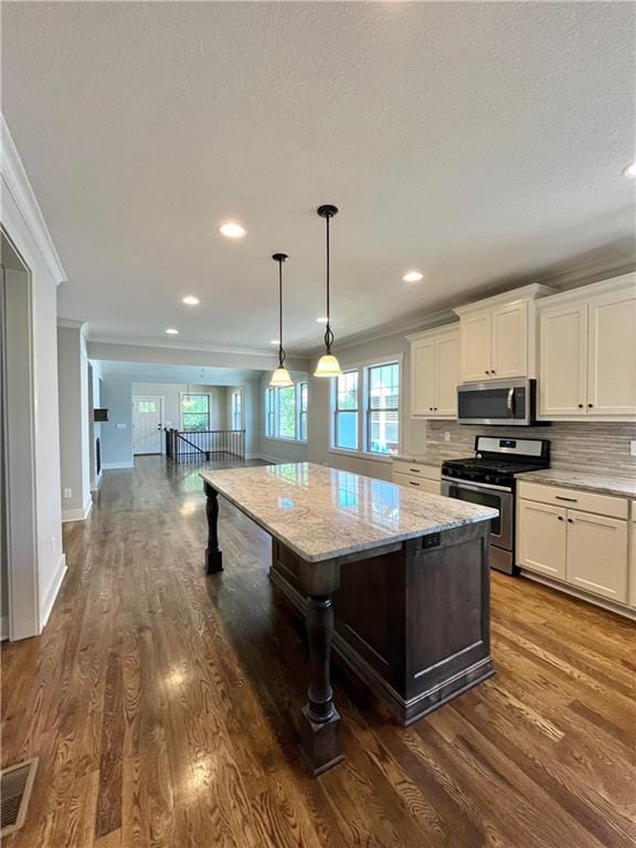 kitchen featuring tasteful backsplash, stainless steel appliances, light stone counters, a kitchen island, and wood-type flooring