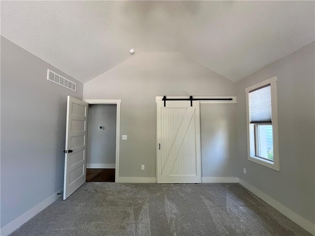 unfurnished bedroom featuring vaulted ceiling, carpet, and a barn door