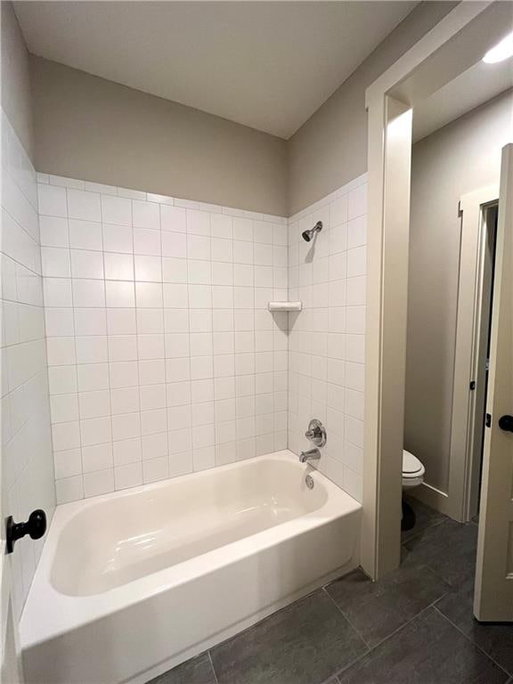 bathroom featuring tiled shower / bath, toilet, and tile patterned floors