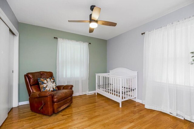 bedroom with a closet, ceiling fan, light wood-type flooring, and a nursery area