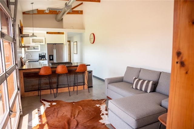 living room with concrete flooring, high vaulted ceiling, beamed ceiling, and sink