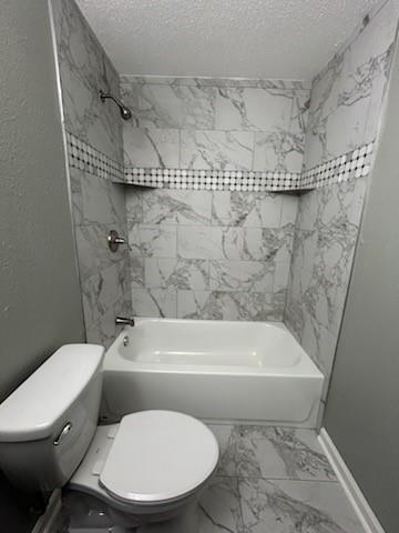 bathroom with tile patterned floors, tiled shower / bath combo, a textured ceiling, and toilet