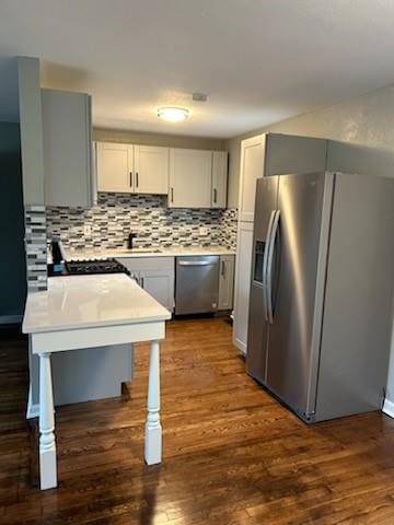 kitchen with tasteful backsplash, appliances with stainless steel finishes, dark wood-style flooring, light countertops, and a sink