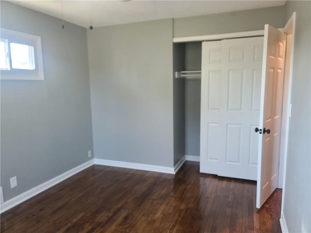 unfurnished bedroom featuring a closet, dark wood-style flooring, and baseboards