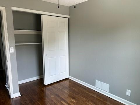 unfurnished bedroom featuring a textured ceiling, wood finished floors, visible vents, baseboards, and a closet