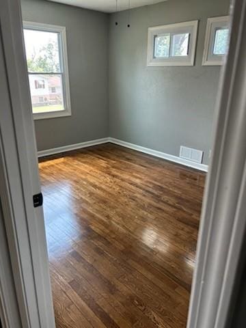 empty room featuring baseboards, visible vents, and dark wood-style flooring