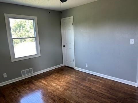 spare room with a ceiling fan, dark wood finished floors, visible vents, and baseboards