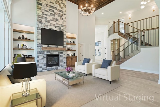 living room featuring an inviting chandelier, a towering ceiling, a stone fireplace, and light wood-type flooring