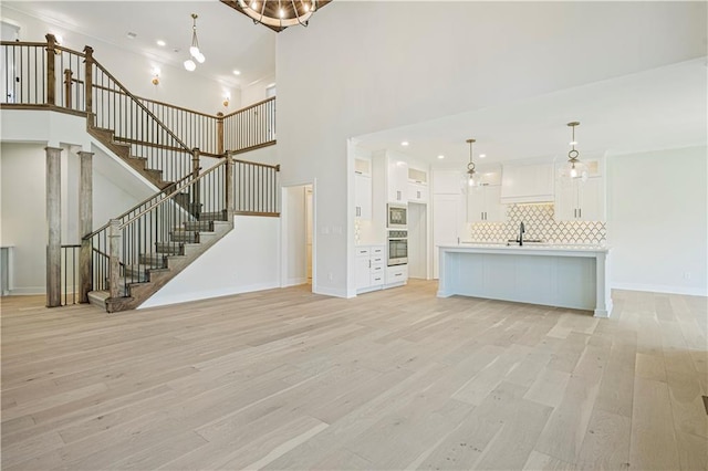 unfurnished living room featuring sink, light hardwood / wood-style floors, and a towering ceiling